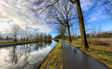 A serene pathway along a tranquil canal, framed by trees and skies, is perfect for relaxation and reflection