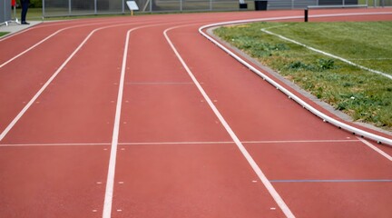 Perspective view of red running track with white lane markings at stadium during daytime