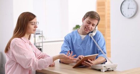 Medical assistant answering phone and helping patient at reception in clinic