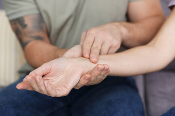 Man checking woman's pulse with fingers at home, closeup
