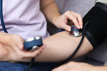Woman checking man's blood pressure with sphygmomanometer on sofa at home, closeup