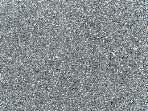 A gray sidewalk surface made of concrete with visible small stones and a rough texture seen outdoors even lighting and a typical urban look without any visible cracks