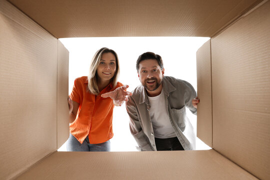 Excited couple looking into cardboard box on white background, view from inside package - Powered by Adobe