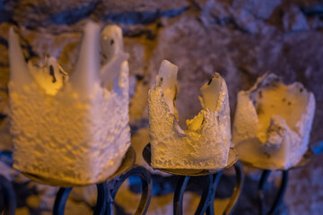 Charred square candles on an old tall candlestick by the wall in the interior of a castle.
