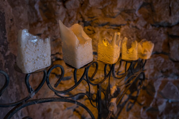 Charred square candles on an old tall candlestick by the wall in the interior of a castle.
