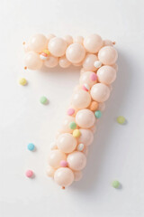 Number seven made of pale color balloons and confeties, isolated on white background. realistic