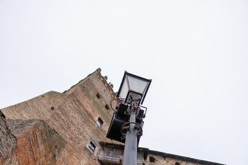A tall stone building rises in the background with bricks and windows. In the foreground, a street lamp stands tall under an overcast sky