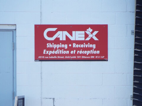 Orleans, ON, Canada-July 4,2025:A red sign for "CANEX Shipping & Receiving" is mounted on a white brick wall, featuring bilingual text and address on Cyrville Rd.