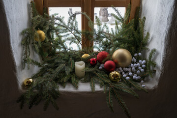 A Christmas decoration with a candle by a wooden window in an interior.
