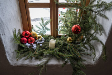 A Christmas decoration with a candle by a wooden window in an interior.
