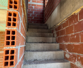 Unfinished concrete staircase in red brick building with exposed walls.