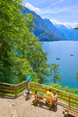 Sch&ouml;ner Panoramablick auf den K&ouml;nigssee, mit Touristen in einem kleinen Ruderboot, und Ausflugsboot.