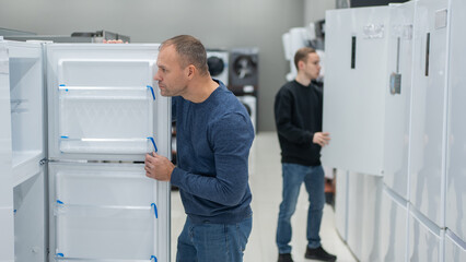 Two Caucasian men are choosing a refrigerator in a hardware store.