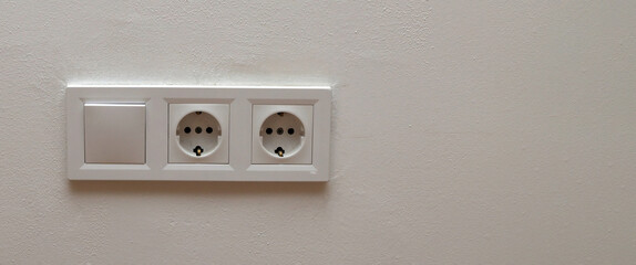 Double electrical wall socket with light switch on white wall