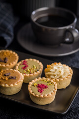 Sweet mini tartlets on plate on black table.