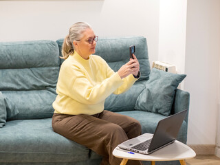 Elderly woman engaged in video call while sitting comfortably at home in cozy sweater
