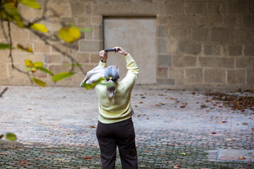 Elderly woman capturing memories during a quiet autumn day in a charming stone courtyard
