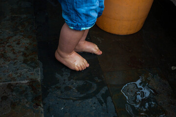 Cute feet of toddler, wet playing with water. with bucket on it's side