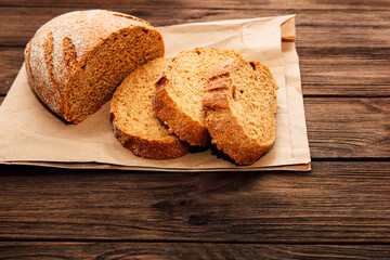 Naklejka premium Freshly baked bread on brown paper with slices on wooden table for a simple meal