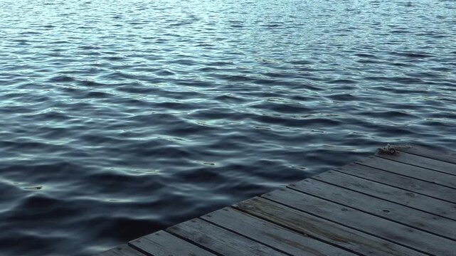 A peaceful close-up of a weathered wooden dock stretching over a calm blue lake. Gentle ripples in the water create a serene mood perfect for nature, travel, and relaxation themes.