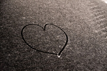 Valentine's Day concept: hand-drawn heart pattern on a frozen car windshield. Hand drawn heart shape on windshield of the car. Love symbol. Romantic background. A frozen windshield with a heart. 