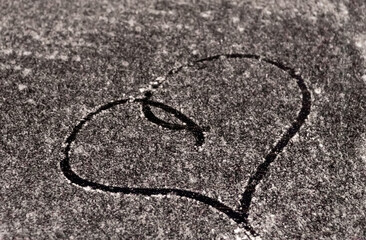Valentine's Day concept: hand-drawn heart pattern on a frozen car windshield. Hand drawn heart shape on windshield of the car. Love symbol. Romantic background. A frozen windshield with a heart. 