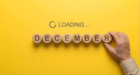 Hand arranging wooden blocks to spell December on yellow background