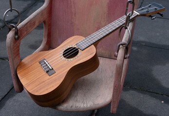 Acoustic wooden ukulele resting on a worn swing seat. Musical instrument in a playground setting. Outdoor leisure and hobby concept