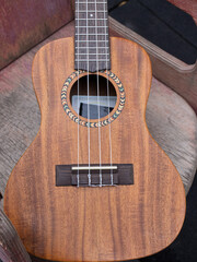 Fototapeta premium Close up of a wooden acoustic ukulele body. Vertical photo of a musical instrument with nylon strings and decorative rosette on a rustic background