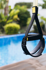 Fitness suspension trainer hanging near a swimming pool, showcasing a sleek design and vibrant colors, ideal for outdoor workout routines and strength training exercises