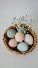 A woven basket contains pastel-colored eggs, including blue, pink, and white. Delicate flowers are arranged around the eggs, symbolizing spring and Easter celebrations.