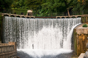 Powerful waterfall flows within Abkhazian city, creating dramatic natural spectacle amid urban landscape.