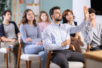 Positive young guy commenting something during a classroom training session in group