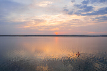 Fototapeta premium Sunset paddleboarder on calm reflective water under colorful sky