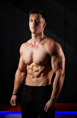 Fototapeta premium Portrait of a sweaty muscular bodybuilder posing on black background.