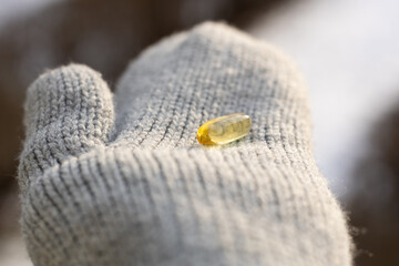 Closeup of a person wearing gloves and holding vitamin D capsules. Concept of supplementing vitamin D in winter.