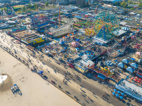 Aerial view of Coney Island's vibrant amusement park, a kaleidoscope of colors and thrilling rides, alongside the sandy beach filled with people, Brooklyn, New York, United States.