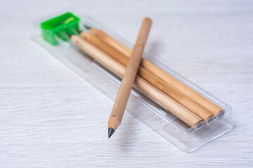 Set of wooden graphite pencils with a green pencil sharpener inside a transparent plastic case on a light wooden surface. School supplies, office stationery and education concept.
