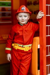 Boy wearing a firefighter costume standing at the entrance of a play fire station in an indoor children&rsquo;s entertainment center. Role play, childhood imagination, learning professions, safe indoor play