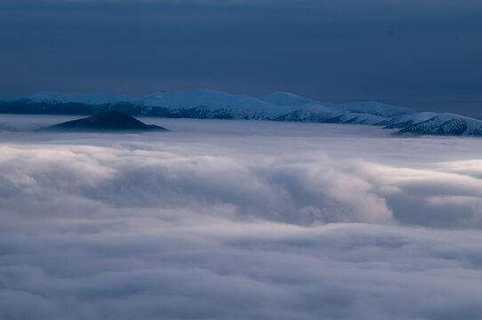 Aerial view of a sea of clouds enveloping the Rakytov mountains, with snow-capped peaks piercing through the misty blanket, Velka Fatra, Zilina Region, Slovakia.