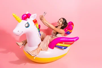 Fotobehang Diamanten Young woman in glamorous pink outfit on a rainbow unicorn inflatable taking a selfie with a phone smiling against a pink background for fashion lifestyle and advertising imagery  © deagreez