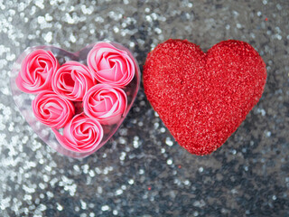 Red heart shaped doughnut and pink roses in a heart shaped container, silver glitter background. Copy space, Tasty sweet pastry food for a special event or Valentine day. Romantic gesture.