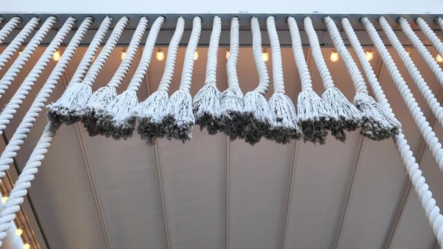 Hanging white ropes and tassels creating decorative ceiling design with light bulbs