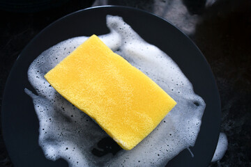 Wet sponge with bubbles dishwashing liquid soaking dishes.