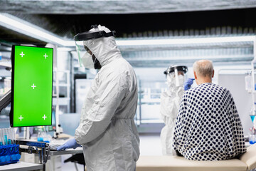 Green screen in vertical position next to doctor in hazmat suit conducting pharmacology experiments and developing vaccines for infection control and biotechnological advancement.