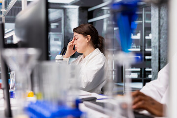 Exhausted laboratory molecular biologist at computer desk processing DNA patient data for clinical research. Stressed lab employee closing eyes, taking break from genetic analysis diagnostics using PC