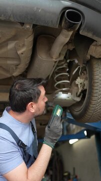 Mechanic inspects car underbody in garage during afternoon work hours