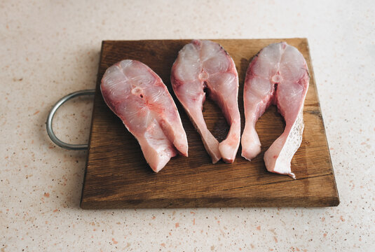 Large, freshly sliced pieces of cleaned silver carp lie on a cutting board on the table. The concept is for preparing a fresh and healthy fish dish.