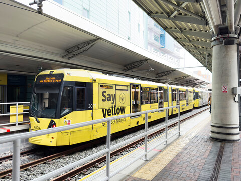 Yellow tram at Manchester station platform in the UK with passengers and modern surroundings