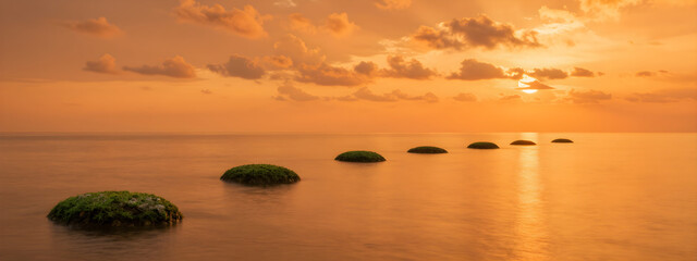 A peaceful sunset reflection on a serene lake shore with vibrant orange hues and fluffy clouds.
